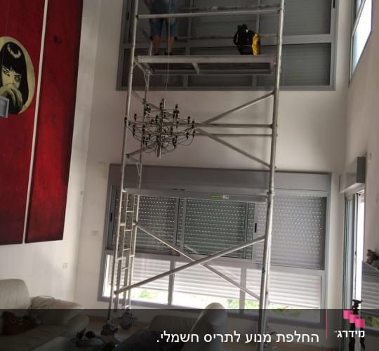 אדם על פיגום מתקין תריסים בחלון גדול